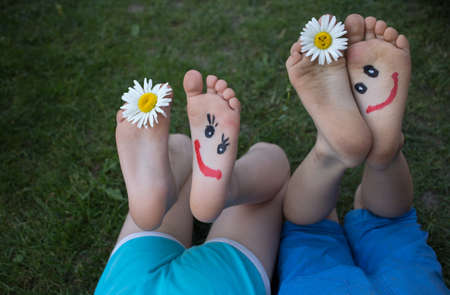 smiling faces painted on the bare feet of two children in shorts lying on the grass. Cheerful childhood. positive atmosphere, hello summer. friendship dayの写真素材