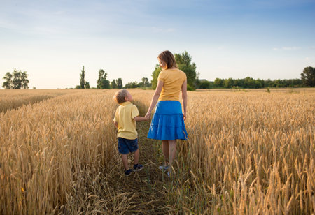 mother and son son in mother's arms walk holding hands among spikelets in a wheat field. enjoy nature and life. Countryside, agriculture, farming. earth day. Harvest in Ukraineの写真素材