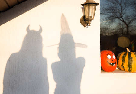 on a light wall, two shadows of silhouettes of people in festive costumes, preparing for a Halloween party. street decor, painted pumpkins on the windowsillの写真素材