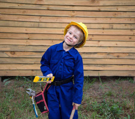 cute inquisitive boy in a blue overalls uniform and a construction helmet with tools in his hands. having fun learning from dad the profession of a builder. little helperの写真素材