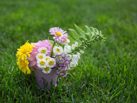 summer flower bouquet of various flowers in a small metal bucket stands on green grass. hello summer. Congratulations on love, positive, beauty and tenderness of natureの写真素材
