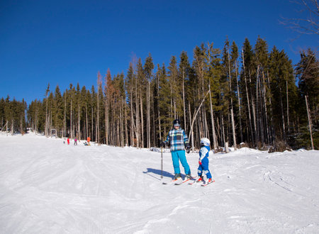 Happy little boy learns to ski with his father during winter holidays in snowy mountains on a sunny cold day. An interesting active holiday with the family. healthy lifestyle, enjoy the momentの写真素材