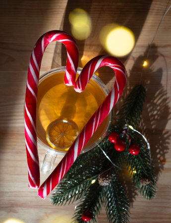 red lollipops stacked in the shape of a heart, lying on a transparent cup with tea, fir branch on a wooden background. top view, selective focus. wishing love in the new yearの写真素材