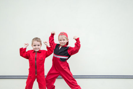 Two cute little boys in red overalls of car service station mechanics, uniform. team work, great service. Work like a dad. Role play and friendship of brothersの写真素材