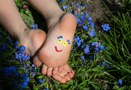 smiling funny face is drawn on children's bare feet lying among small blue flowers. Children of Ukraine against the war. positive atmosphere, happy childhood. Hello summer, day of smiles. Humorの写真素材