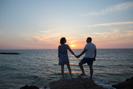 man and woman, he and she in full growth, silhouettes of couple in love against backdrop of sea and sunset stand holding hands. enjoyment of the moment, tender feelings, pleasant pastimes. Valentine's Dayの写真素材
