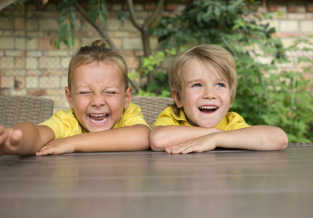 face portrait of two cute laughing boy 5 years old . Happy childhood, positive emotions, joy, jokes. Children, brothers sit at the table and have fun. Communication with friends during the holidaysの写真素材