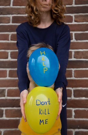 two unrecognizable people, adult and child, with blue yellow balloons with inscriptions do not kill me and help. Ukrainians are against war. Fear, drawing attention to military conflict in Ukraineの写真素材