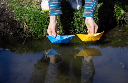 female hands launch paper boats of yellow and blue colors of the Ukrainian flag into the water. Symbol of freedom, independence. Drawing attention to the war in Ukraine. Patriotic children gamesの写真素材