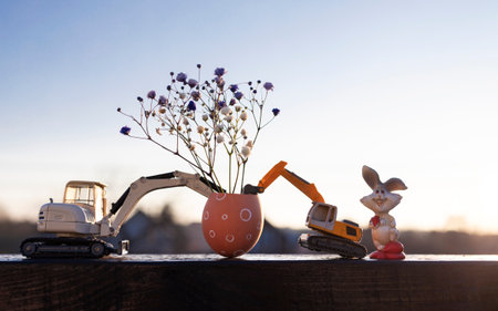 two models of toy excavators, an eggshell with flowers in it, an Easter bunny in the backlight at...