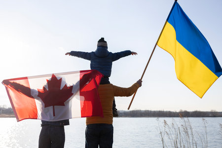 family with a child with Ukrainian and Canadian flags stand together in nature. International...