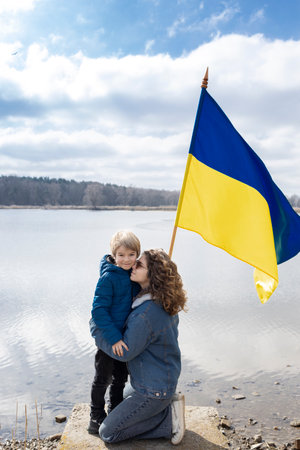 boy and young woman, little brother and adult sister, next to lake with flag of Ukraine. Family, unity, refugees, support. stand with Ukraine. stop war with Russia. problems of refugees and immigrantsの写真素材