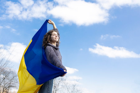 an adult girl of 18 years old, holds a Ukrainian yellow-blue flag behind her back against the sky, looks ahead, in the hope of a brighter future. Ukrainians are against the war. Support Ukraineの写真素材
