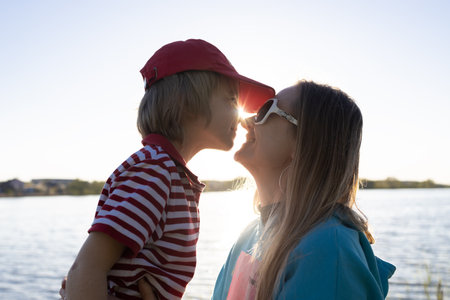 close-up of mother and son face to face in backlight of the setting sun on the lake. enjoyment of the moment, tender feelings, pleasant pastime. Positive human emotions, happy motherhood. mother's dayの写真素材