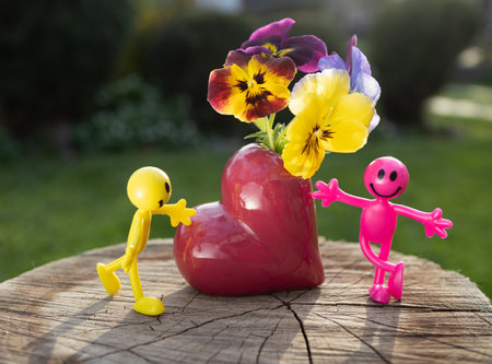 Miniature bright toy figures of men near a heart-shaped vase with pansies. couple in love and the concept of romance, love and tender feelings. happy relationshipの写真素材