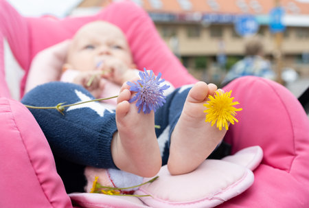 Detail of small infant feet lying in stroller. bare feet of baby and flowers between his toes. positive atmosphere, air baths, carelessness, peace, happy childhood. Explore the world. selective focusの写真素材