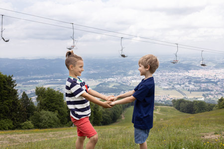 Two boys of 7 years old are standing on the slope of low mountains, holding each other's hands. Healthy lifestyle, weekend hiking, support and friendship, active summer holidays. natural landscapeの写真素材