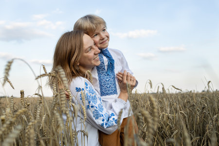 joyful boy and woman in vyshyvanka hug each other among spikelets in a wheat field. Ukrainian family, unity, support, stand with Ukraine. Independence Day of Ukraineの写真素材