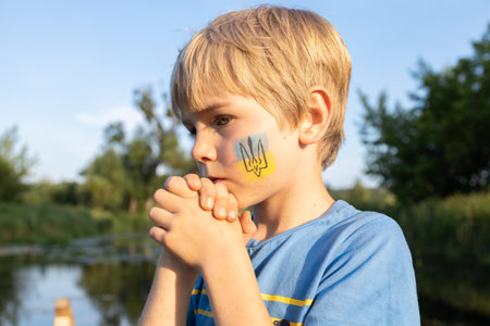 unhappy sad boy with a painted trident on his cheek. Children against war. Ukrainian child asks for...