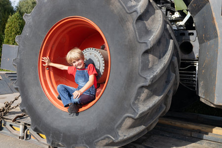 boy sits in a huge tractor wheel, looks into the frame, smiles. Male hobbies. Passion for large...