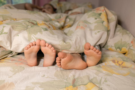 two children sleep in bed. bare, clean feet of siblings, lying side by side under the same blanket on the bed. morning relaxation, cozy rest, childish tenderness, family joy. cute pictures of baby feetの写真素材