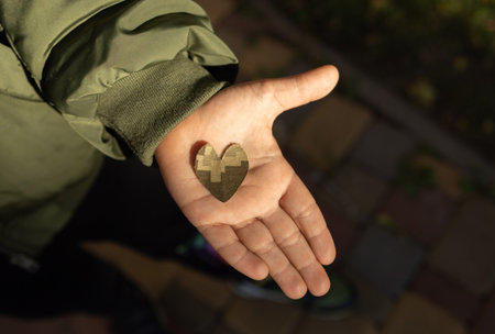 heart cut from camouflage fabric on child palm illuminated by sun. Stop war in Ukraine. With love...