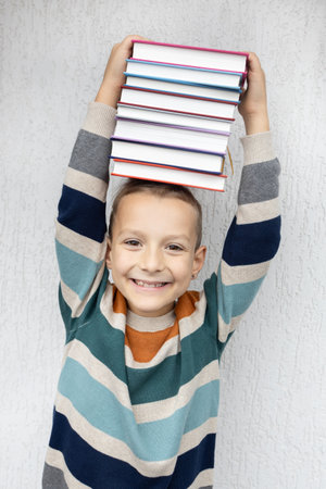 cheerful cute boy of 8 years old holds a stack of books on his head. back to school. Book Day. Read...