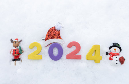 Christmas, New Year, festive mood. multi-colored numbers 2024 and souvenir miniature figurines of a deer and a snowman in the snow. Time to make wishes. Winter holiday cardの写真素材
