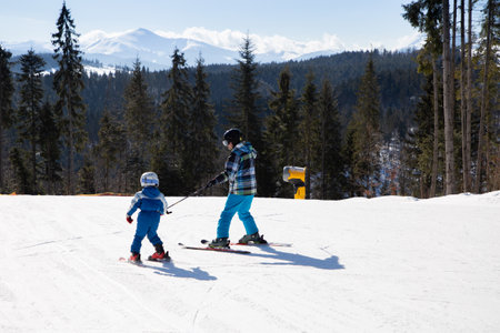 Children's skiing lesson at ski school. Seasonal joys, happy childhood. Frosty weather. workout. healthy lifestyle little boy learning to ski with his father in the snowy mountains on sunny cold dayの写真素材