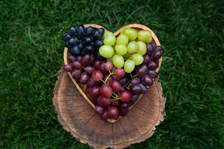 heart-shaped plate with colorful, tasty, ripe grapes. bunches with large berries of pink, blue, green grapes, collected for tasting in the vineyardの写真素材