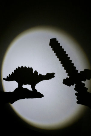 interesting contrasting shadows on the wall from a toy dinosaur and a sword. Games with light and shadow. happy cheerful childhood, ideas for evening family time, lifestyle, imagination developmentの写真素材