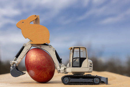 gray small toy excavator and an Easter egg against the sky. Easter holiday concept for construction companiesの写真素材