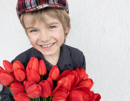 cute boy 6 - 7 years old with a large bouquet of red tulips on a light background. Mothers Day....