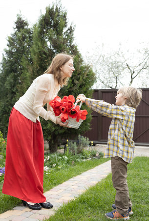 Mother's day, birthday. The atmosphere of family love, tenderness of relationship between mom and son. Happy motherhood. cute 6 year old son hands his mother a bouquet of tulips in a basketの写真素材