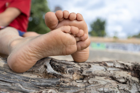 Bare feet child lying on a sandy beach. Cute toys and heels. Summer holidays and healthy lifestyle conceptの写真素材