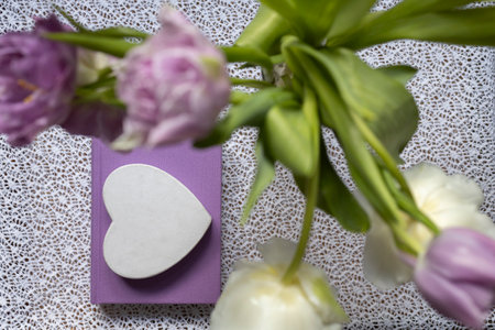 Top view of tulip flowers standing on the table, a lilac book and a white heart on it. concept of loving reading, self-education, aesthetics. Cozy morning atmosphere, holiday giftの写真素材