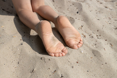 The child's bare feet lie on the warm sand. Carefree childhood, the joy of summer. holidays and...