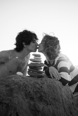 black and white photo of guy and girl, young couple in love kissing. in front of them stands balancing tower of stones. concept of love, relaxation, search for life harmony. Spending time togetherの写真素材
