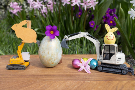 model of a toy excavator, large and small multi-colored Easter eggs on a background of spring blooming flowers. Easter spring holiday concept for construction companies. Business cardの写真素材
