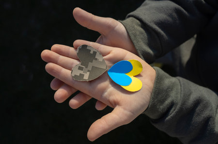 heart cut out of military camouflage fabric and yellow blue paper lies on childs palm. Stop war in...