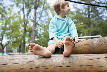 barefoot boy 6-7 years old sits on a tree trunk on a summer day. Walking barefoot in nature in summer is a pleasure. activities for children in the park. Focus on children's feetの写真素材