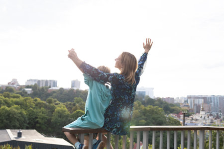 mother and son sit together on the railing against the background of the sky and the cityの写真素材