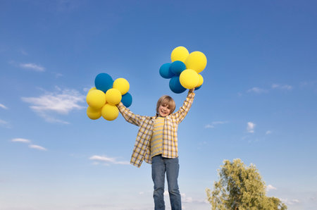 Full-length photo of happy boy holding many yellow and blue balloons against the sky. feels great, festive, birthday. Independence Day of Ukraine. Balloon Dayの写真素材