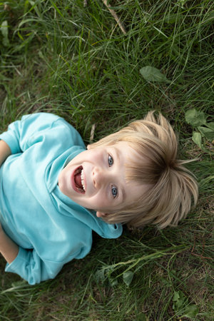 face of a cute cheerful boy lying on the green grass, top view. enjoying nature in the fresh air....
