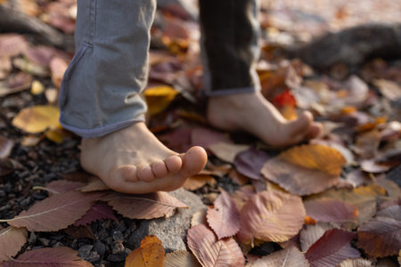 barefoot child walks through colorful fallen dry leaves in an autumn park. carefree childhood, freedom, relaxation, walking, enjoying the warm autumn. exercises for healthy feet. Indian summer.の写真素材
