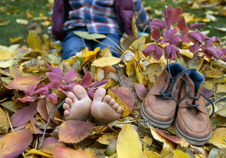 child took off his shoes and covered bare feet with colorful dry leaves in autumn park. freedom, relaxation, walks, enjoying the warm autumn. positive atmosphere, happy childhood, children in natureの写真素材
