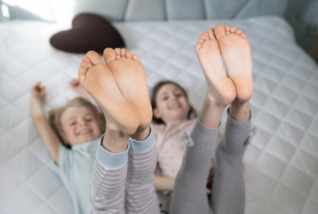 Two cheerful children playing around while lying on bed, cheerfully raised up bare feet. focus on...