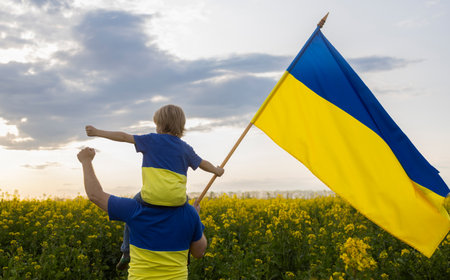 son, sitting on dad s shoulders, in yellow and blue T-shirts, with flag of Ukraine among blooming rapeseed field. patriotism, pride, unity, Independence Day, dream of victory for Ukraine. Stop warの写真素材