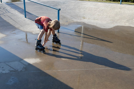 boy joyfully rides on roller skates at speed through puddle on asphalt after rain, splashing water...