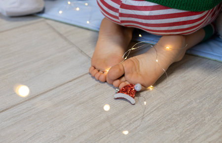 child's bare feet on the floor, a garland, a small decorative Santi hat. selective focus. Cozy...
